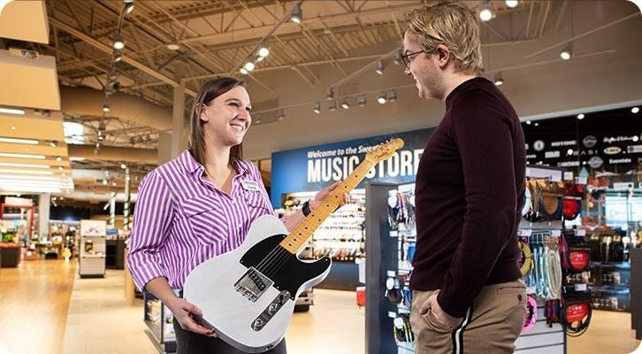 Foto: Steele Solid, tecnico delle vendite di un negozio di musica, aiuta un cliente con una Fender Telecaster.