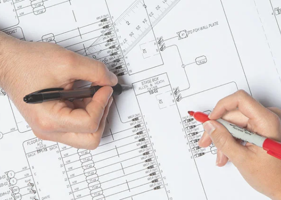 A pair of hands each with pens, drawing on schematics